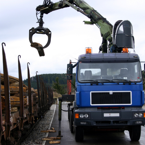 Crane Rental Services Blue truck with crane lifting wooden logs on a road