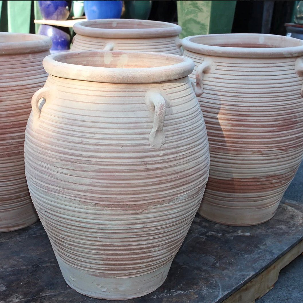 Three terracotta pots with ribbed texture and handles on a stone surface.