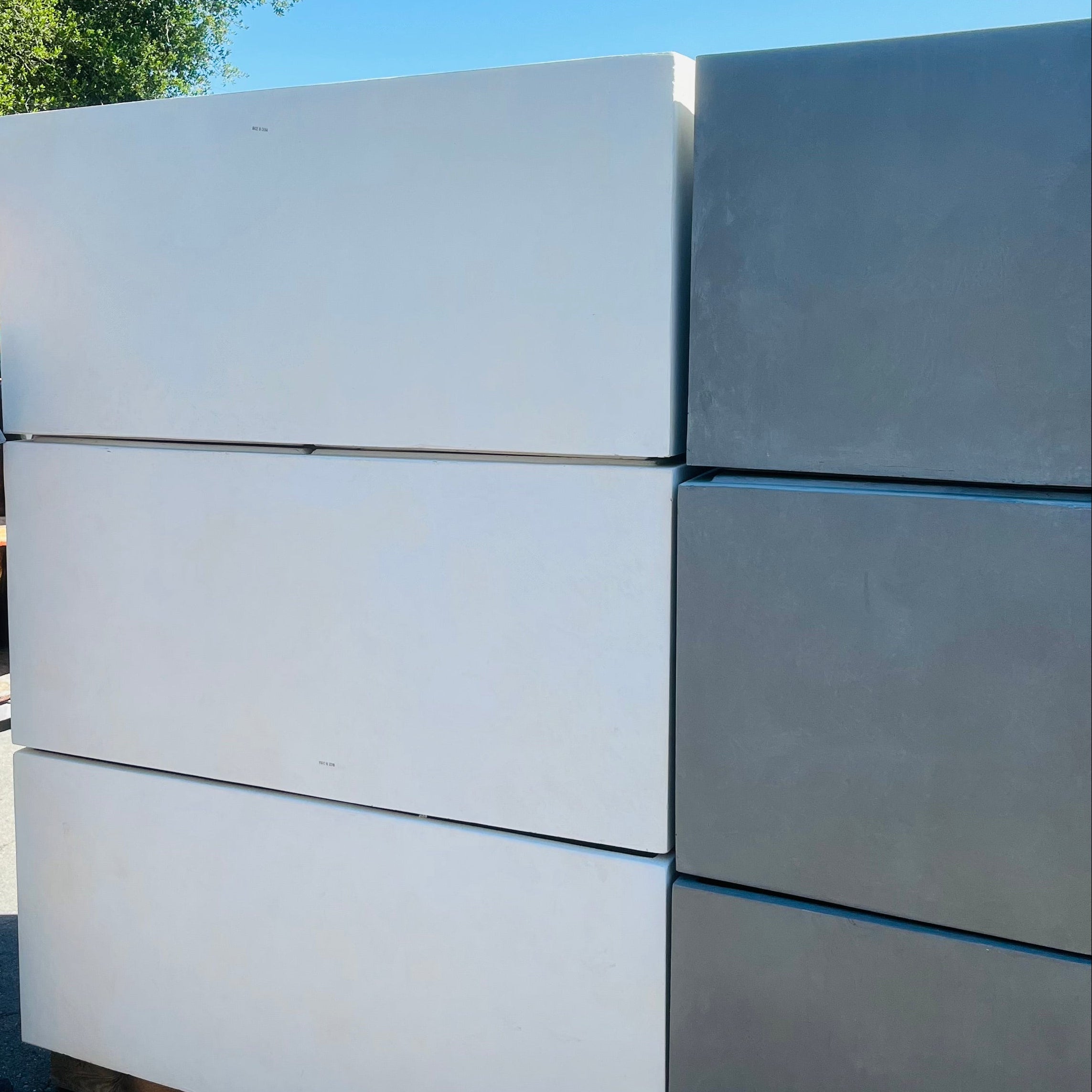 Person standing next to a stack of large white and gray concrete blocks with a yellow vehicle in the background.