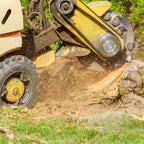 Tree stump grinder in action on a tree stump with grass and dirt in the background.