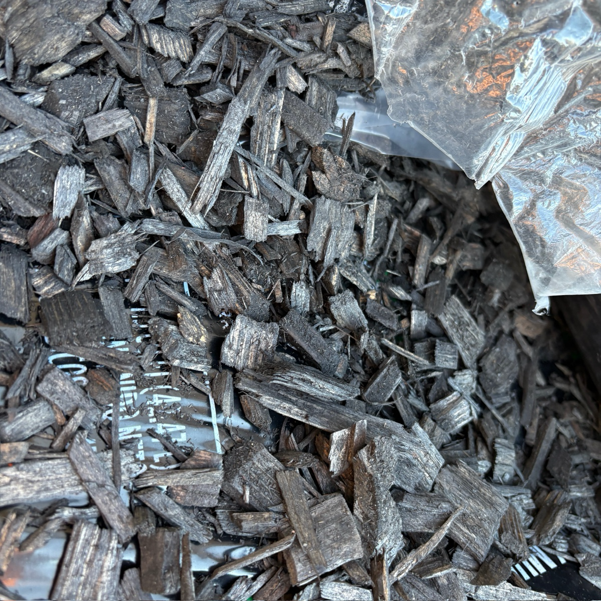 Close-up of dark wood chips with a clear plastic bag partially visible.