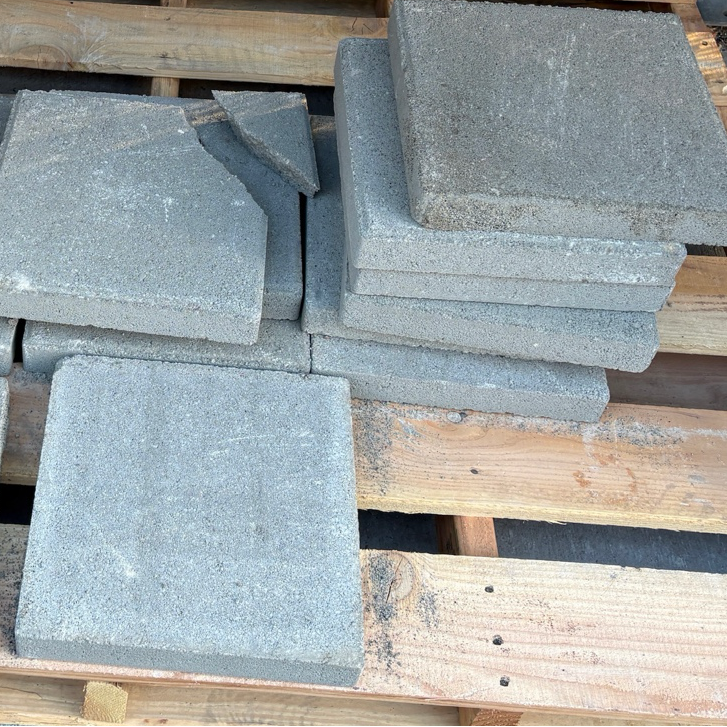 Pile of gray square stones on a wooden pallet with a background of bricks and a display board.